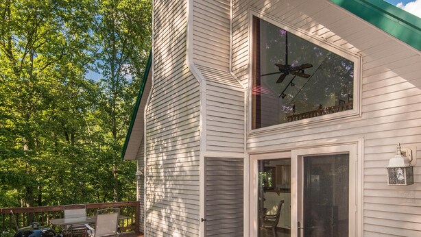 A two-story house with a deck, a chimney, and a large window. - Private Chalet Near State Forest | Game Room, Fire Pit & Views (Unionville)
