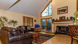 A spacious living room with a brown leather sofa, a television, and a fireplace. - Private Chalet Near State Forest | Game Room, Fire Pit & Views (Unionville)