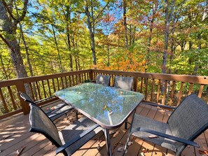 A wooden deck with a glass table and four chairs.