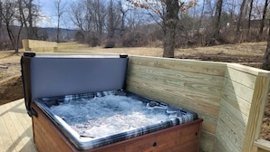 A hot tub with a wooden exterior, a bench, and a wooden deck.