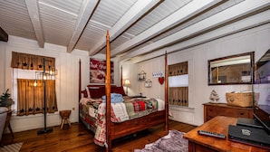 A bedroom with a four-poster bed, wooden flooring, a desk with a laptop, and a large mirror.