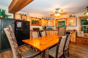 A kitchen with wooden cabinets, a black refrigerator, a dining table with chairs, and a ceiling fan.