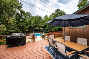 Um deck de madeira com piscina, móveis de exterior e churrasqueira coberta.