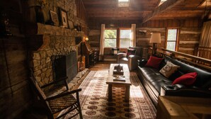 L’intérieur d’un chalet rustique en rondins de bois, avec une cheminée en pierre, un canapé en cuir et une table à manger en bois.