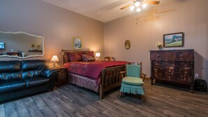 A bedroom with a bed, a wooden dresser, a green chair, a black leather couch, and a ceiling fan. - Cowboy Guest Suite | Near Trails, Events & Music Barn 1BR, 1BA (Nashville)