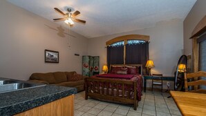 A bedroom with a bed, a wooden headboard, a nightstand, a desk, and a chair. There is a window with curtains, a ceiling fan, and a picture on the wall. - Cowgirl Guest Suite | Near Trails, Events & Music Barn 1BR, 1BA (Nashville)