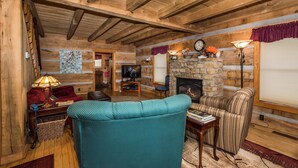 A cozy log cabin interior with a stone fireplace, wooden beams, a television, and comfortable seating. - Secluded Log Cabin | Hot Tub, Fireplace & Near Nashville 2BR, 1.5BA (Nashville)