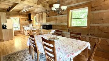 Un intérieur en bois comprenant une table à manger, des chaises, un lustre et un coin cuisine.