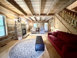 A log cabin interior with a stone fireplace, a red couch, and a wooden staircase. - Secluded Log Cabin | Hot Tub, Fireplace & Near Nashville 2BR, 1.5BA (Nashville)