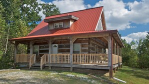 A log cabin with a red metal roof, wooden porch, and a small front door. - Secluded Log Cabin | Hot Tub, Fireplace & Near Nashville 2BR, 1.5BA (Nashville)