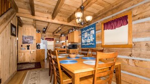 A wooden cabin interior with a dining area, kitchen, and a large window with a curtain. - Secluded Log Cabin | Hot Tub, Fireplace & Near Nashville 2BR, 1.5BA (Nashville)