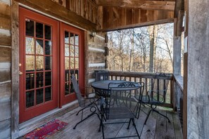 Eine Holzhütte mit roter Tür, einer Veranda mit Tisch und Stühlen und Blick auf Bäume.