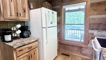 Une cuisine de style rustique, avec des éléments en bois, comprenant un réfrigérateur, une machine à café et une fenêtre donnant sur une terrasse.
