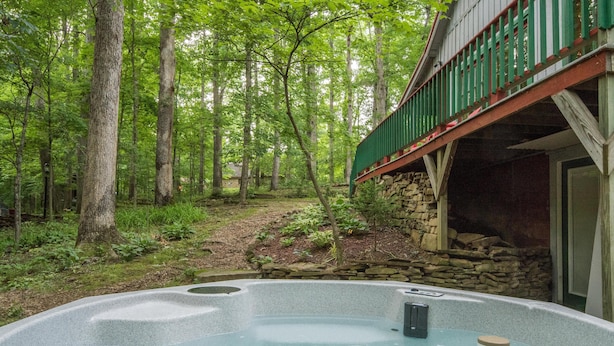 A hot tub in a forested area with a stone wall and a wooden deck. - Hilltop Cabin 2 Miles to Nashville | Hot Tub & Valley Views 2BR, 2BA (Nashville)