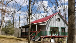 A rustic cabin with a red roof, white walls, and green trim. It features a porch with a red railing and a staircase leading to the entrance. - Hilltop Cabin 2 Miles to Nashville | Hot Tub & Valley Views 2BR, 2BA (Nashville)