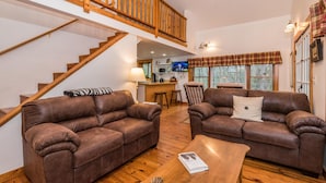 A spacious living room with two brown leather sofas, a wooden coffee table, and a staircase leading to an upper level. - Hilltop Cabin 2 Miles to Nashville | Hot Tub & Valley Views 2BR, 2BA (Nashville)