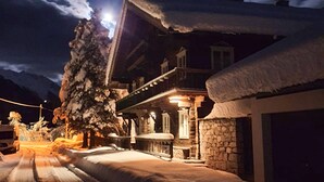 A snow-covered building with a stone facade and a balcony, under a night sky with a visible moon.