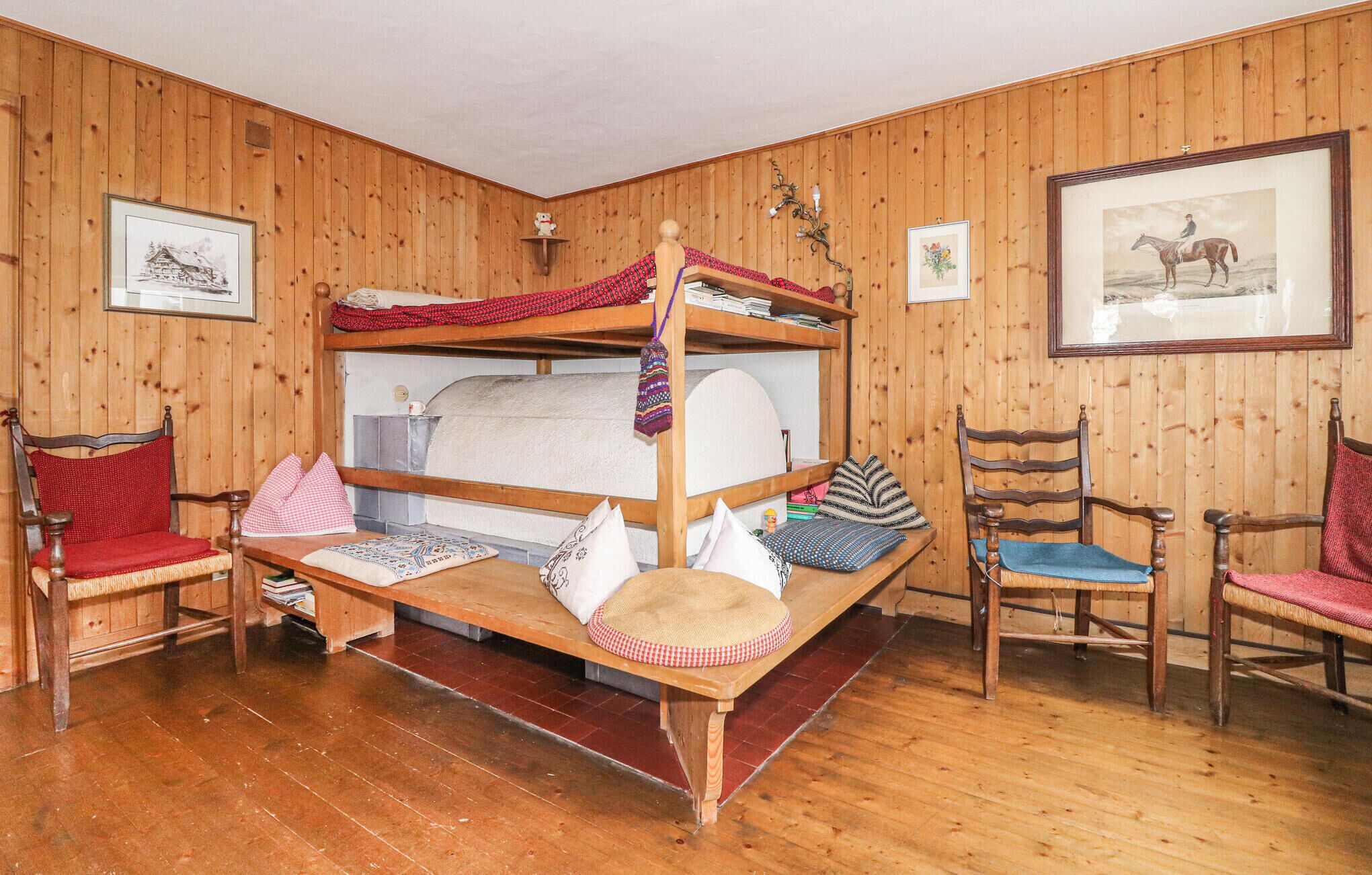 Ein gemütliches Zimmer mit Holzwänden und Holzdielen, ausgestattet mit einem Etagenbett, zwei Holzstühlen, einem kleinen Tisch und gerahmten Bildern an der Wand.