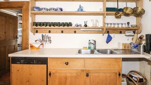 A kitchen with wooden cabinets, a built-in dishwasher, and a variety of kitchen utensils and cookware on shelves.