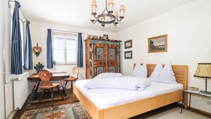 A bedroom with a wooden bed, a desk, a chair, a wardrobe, a chandelier, and a rug.