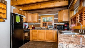 Una cocina con armarios de madera, un refrigerador negro, encimeras de granito y un ventanal con persianas.