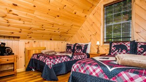 Un dormitorio acogedor con paredes de madera y techo inclinado. Hay dos camas con colchas estampadas y una mesita de noche con un oso de peluche.