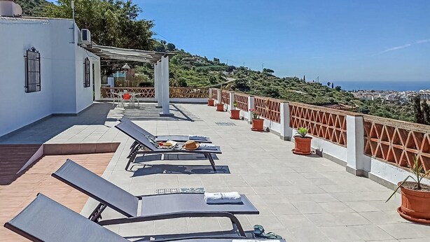 Um terraço com espreguiçadeiras, uma pérgola e vista para a cidade e o mar.