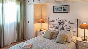 Cama bem arrumada com roupa de cama estampada, duas luminárias de cabeceira, um criado-mudo e um guarda-roupa com várias portas.