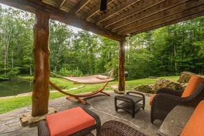 An outdoor patio with wicker furniture, a hammock, and a view of a forested area. - Secluded Log Cabin w/ Pond, Hot Tub & Game Room 3BR, 3.5BA (Nashville)