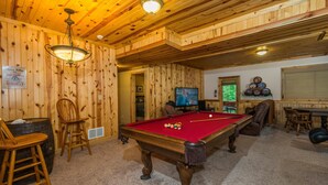 Ett biljardbord i ett rum med träpanel på väggarna och i taket, en tv och en skylt som visar att det finns en whiskybar i närheten.