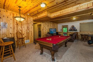 A pool table in a room with wooden walls and ceiling, a television, and a sign indicating the presence of a whiskey bar.