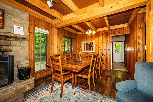 A wooden dining room with a large table and chairs, a stone fireplace, and a view of the outdoors through large windows. - Secluded Hilltop Cabin | Hot Tub, Pool Table & Near Nashville 4BR, 3BA (Nashville)
