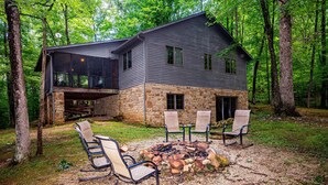 Une maison moderne avec des fondations en pierre et une grande terrasse, entourée d’une forêt.