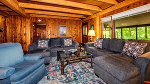 Un salon chaleureux avec des murs et un plafond en bois, une grande fenêtre et un canapé bleu.