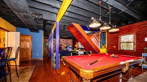 A pool table with a red felt surface, surrounded by wooden chairs and a pool cue. - Private Lake Lodge | 21 Acres, Hot Tub & Game Room 5BR, 2.5BA (Morgantown)