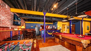 A billiards room with a pool table, foosball table, and a bar area with stools and a television screen. - Private Lake Lodge | 21 Acres, Hot Tub & Game Room 5BR, 2.5BA (Morgantown)