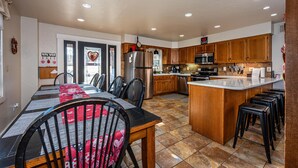 A spacious kitchen with wooden cabinets, a central island, and a dining area with a table and chairs. - Private Lake Lodge | 21 Acres, Hot Tub & Game Room 5BR, 2.5BA (Morgantown)