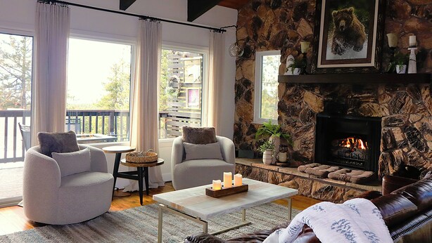 A cozy living room with a stone fireplace, two armchairs, a coffee table, and a view of the outdoors.