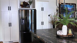 A kitchen with white cabinets, a stainless steel refrigerator, a marble countertop, and a painting on the wall.