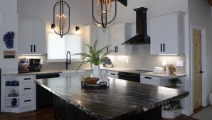 A modern kitchen with white cabinetry, a large island, and a black range hood.