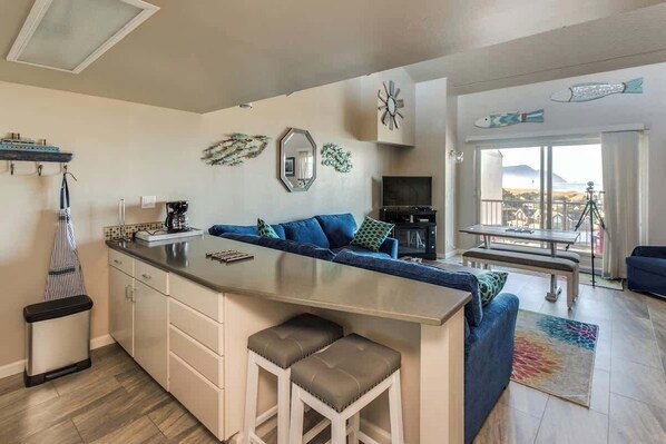 A modern kitchen with a central island, a dining area with a bench, and a balcony with a view.