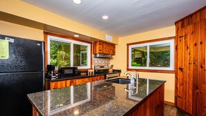 A kitchen with granite countertops, wooden cabinets, a stainless steel refrigerator, and a window overlooking greenery. - 85-Acre Family Cabin | Sleeps 12, Hot Tub & Near Nashville 4BR, 2 BA (Nashville)