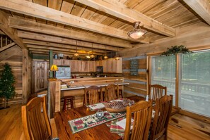 A rustic wooden interior with a dining area featuring a wooden table, chairs, and a Christmas tree. - Private 10-Acre Log Cabin | Hot Tub & Near State Park 2BR, 2.5 BA (Nashville)