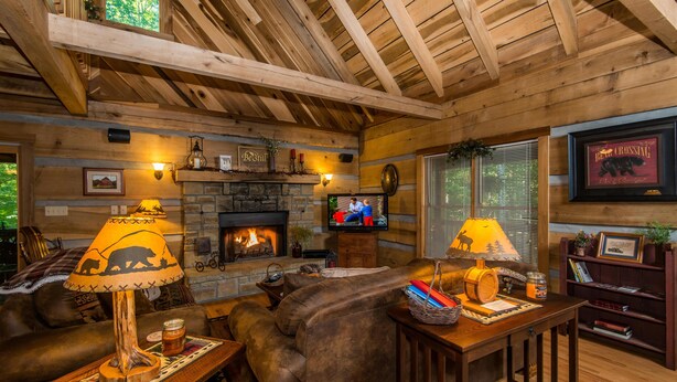 A cozy cabin interior with a stone fireplace, leather sofas, and wooden beams. - Private 10-Acre Log Cabin | Hot Tub & Near State Park 2BR, 2.5 BA (Nashville)