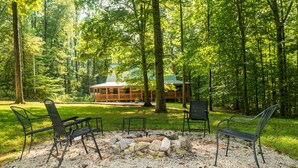 A forested area with a wooden cabin, outdoor seating, and a fire pit. - Private 10-Acre Log Cabin | Hot Tub & Near State Park 2BR, 2.5 BA (Nashville)
