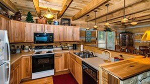 A wooden kitchen with a stove, microwave, and sink. - Private 10-Acre Log Cabin | Hot Tub & Near State Park 2BR, 2.5 BA (Nashville)
