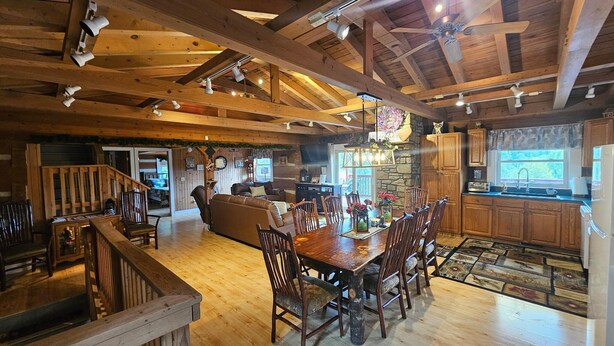A spacious living area with a wooden dining table surrounded by chairs, a fireplace, and a kitchen area with a stone wall and wooden cabinets. - Mountain View Log Cabin | Hot Tub, 3 Kings & Game Room 3BR, 3BA (Nashville)