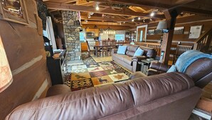 A cozy cabin interior with a stone wall, a fireplace, a dining area, and a living room with leather sofas. - Mountain View Log Cabin | Hot Tub, 3 Kings & Game Room 3BR, 3BA (Nashville)