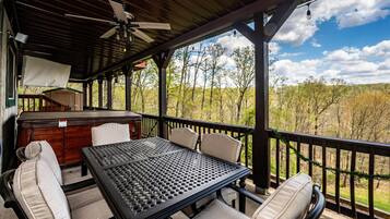 A covered outdoor patio with a table and chairs, a ceiling fan, and a view of trees and hills.
