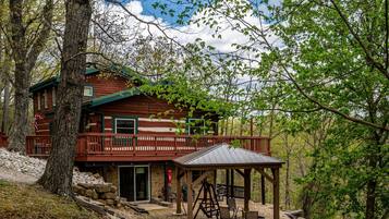 A cabin with a wooden exterior, a balcony, and a covered outdoor seating area.